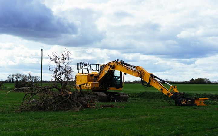 Excavator piling cut brush on an open field