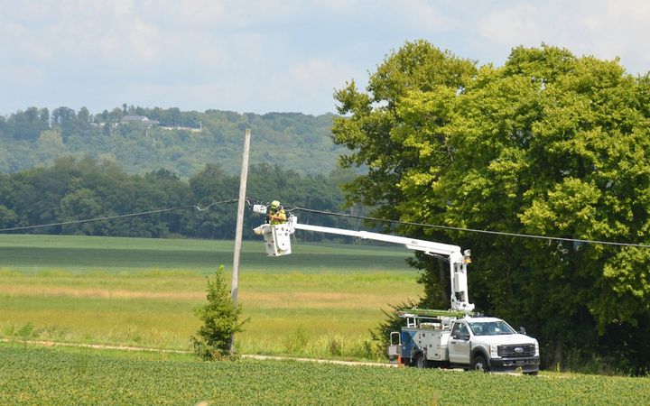 Utility worker in a bucket truck at a power line beside a green field
